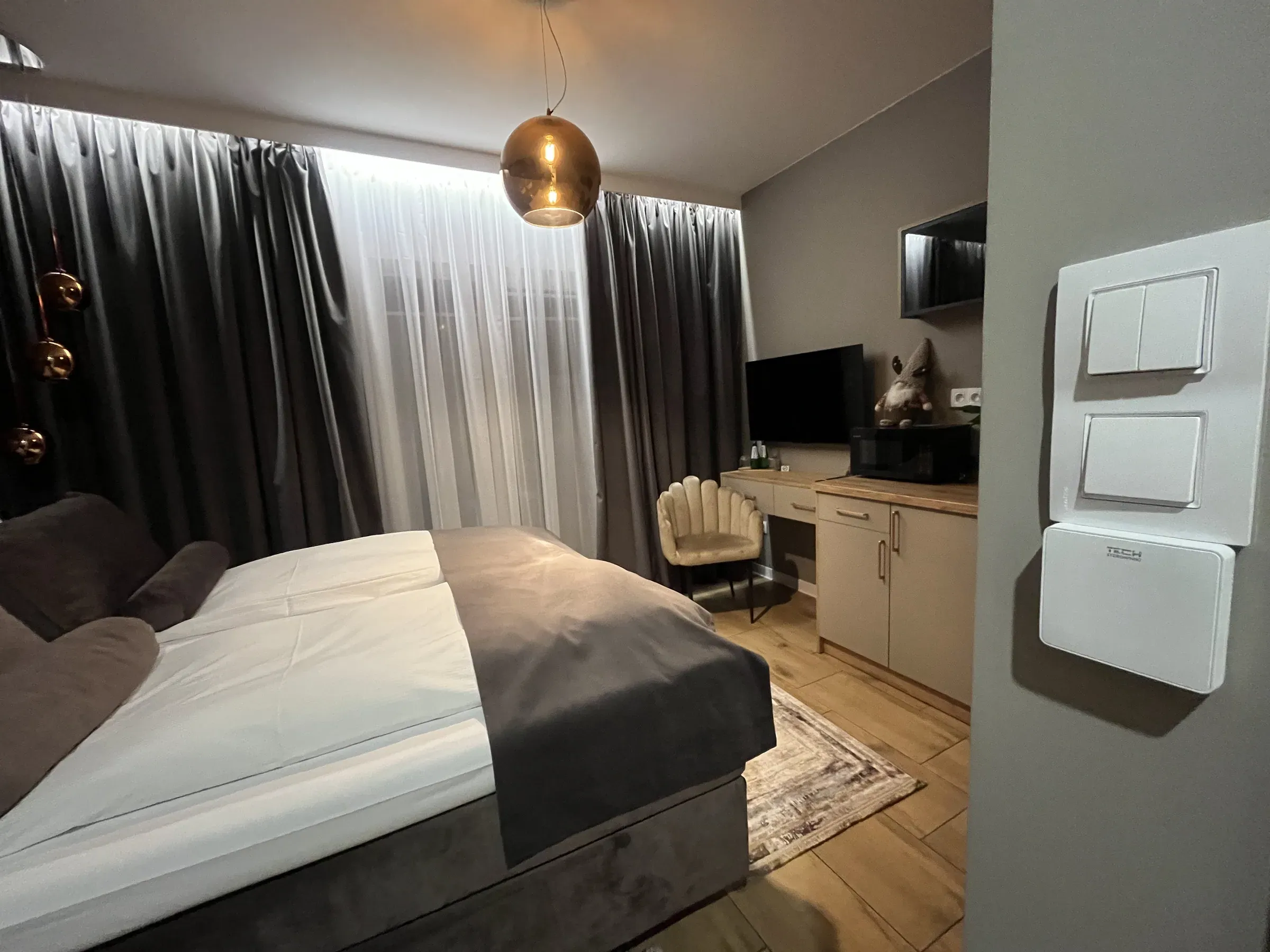 Pokój hotelowy w Raszynie z białym regulatorem temperatury TECH przy włącznikach światła